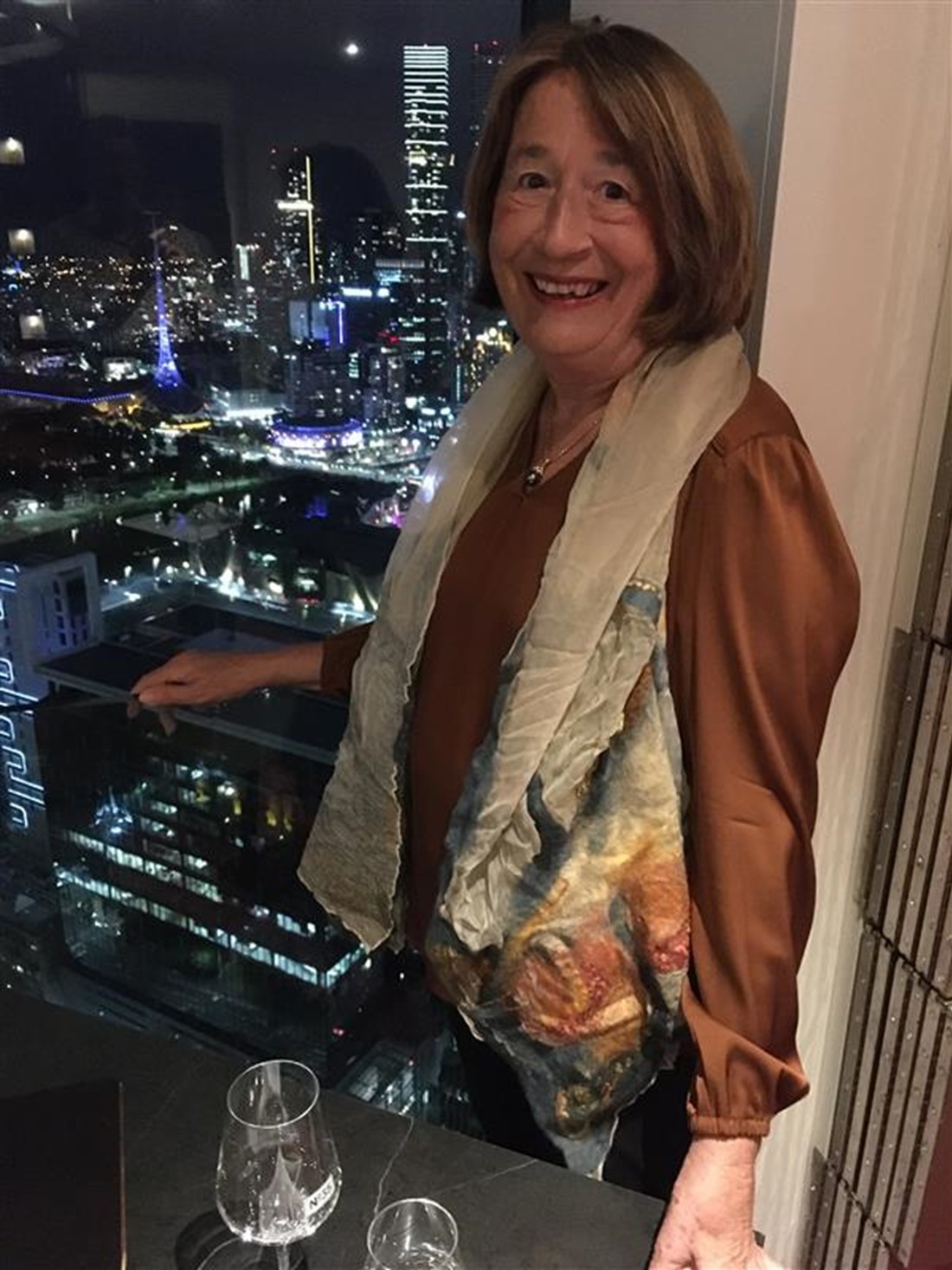 A portrait of Frances smiling in front of a window with city views