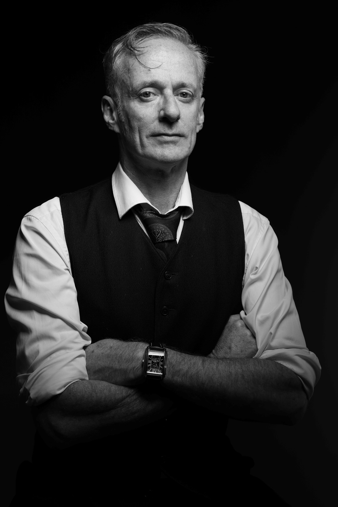 An intimate black and white portrait of Dominic, wearing a formal shirt, tie, and vest, who looks at the camera, with a composed expression on his face.